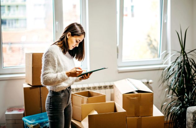 Woman going over a clipboard standing over cardboard boxes.