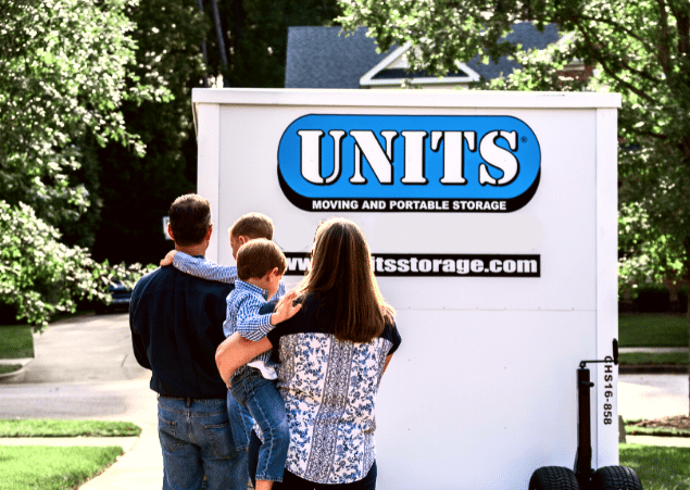 Mother and father each holding one of their young sons, standing in front of their UNITS Moving and Portable Storage container in their driveway.