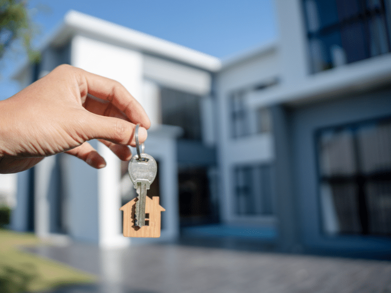 Person holding keys in front of a house.