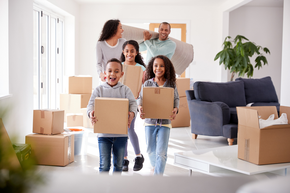 Happy family moving bringing boxes and a rug into their new home.