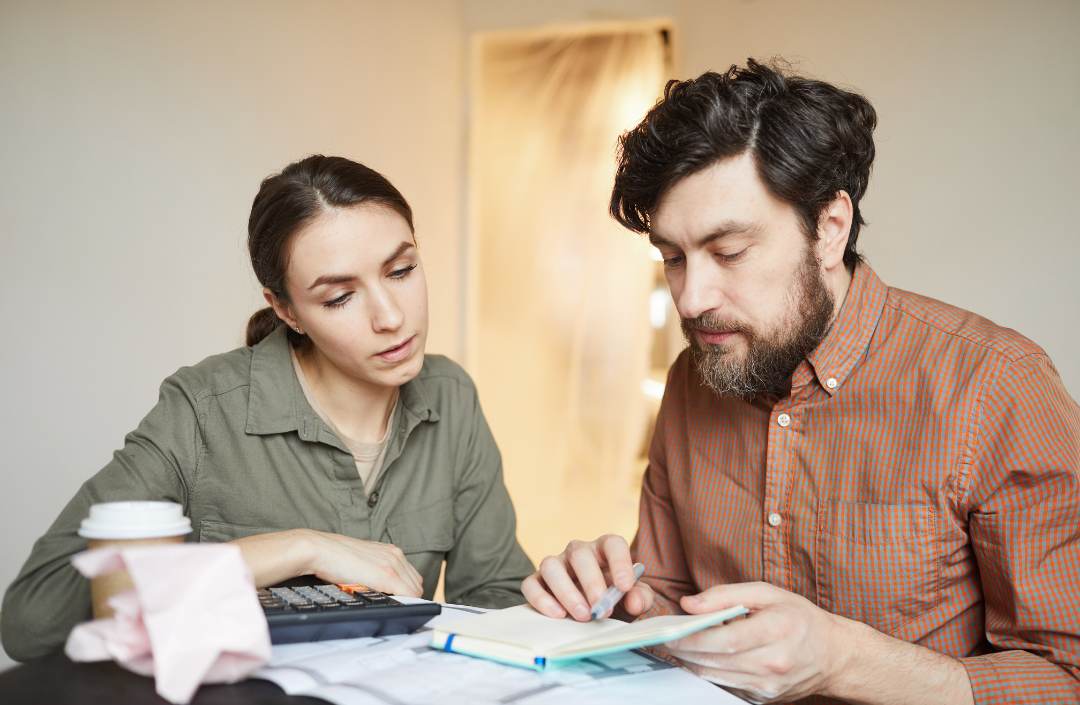 Couple sitting together going over a small book with a calculator out.