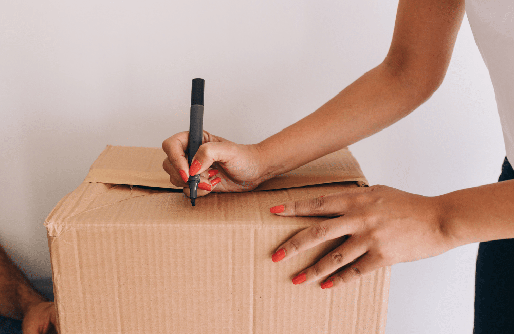 Woman labeling a cardboard box with a marker.