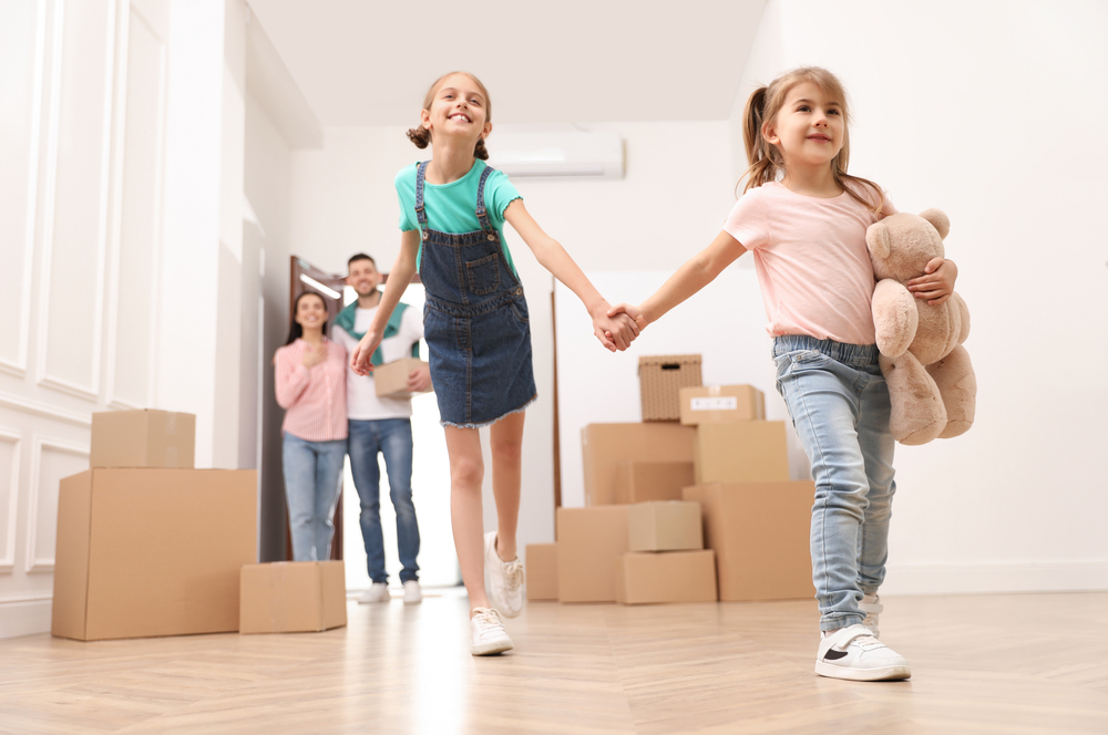 Two young sisters walking through their new home while their parents watch from behind them.