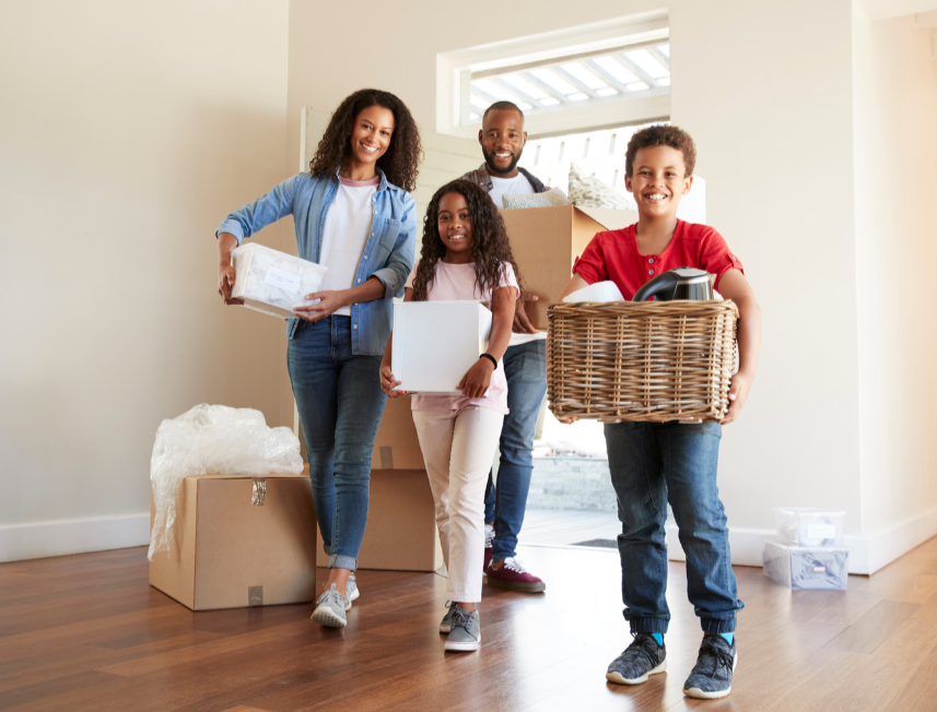 Smiling family carrying their packed belongings through an empty house.