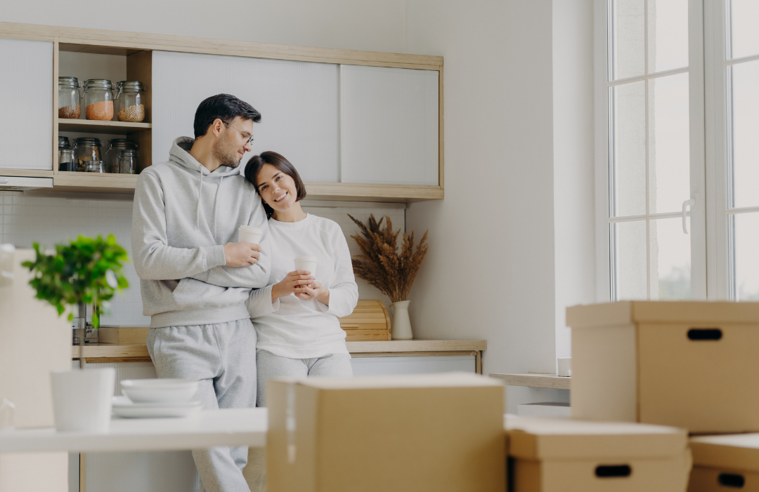 Couple standing in their kitchen looking at cardboard boxes.