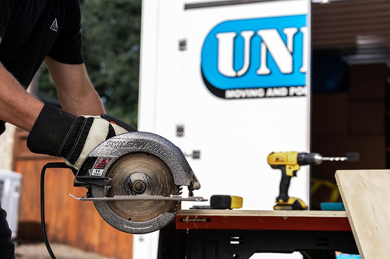 Man sawing through wooden board in front of UNITS Moving and Portable Storage container.