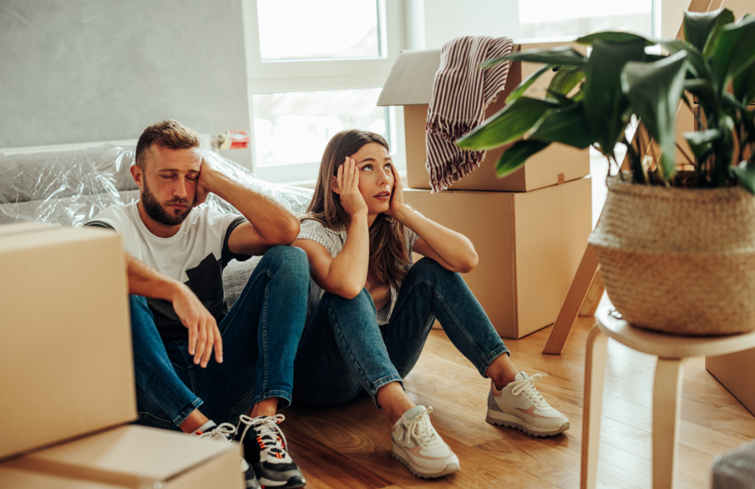 Man and woman exhausted and overwhelmed sitting on the floor surrounded by cardboard boxes.