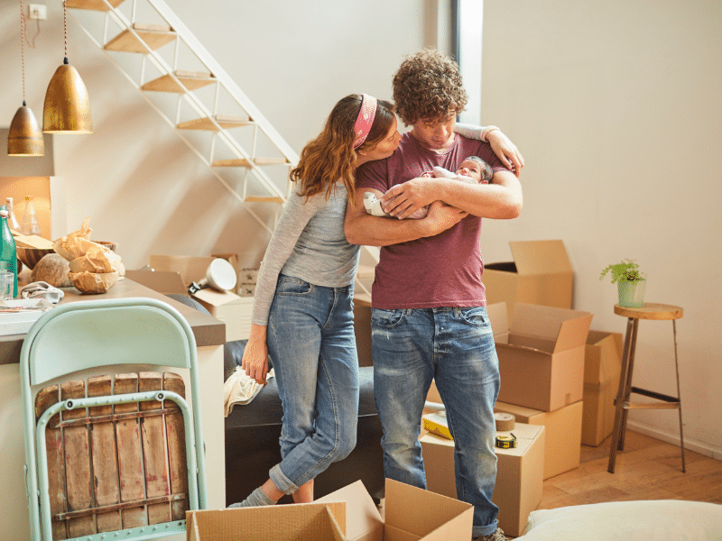 New parents holding their baby surrounded by boxes.